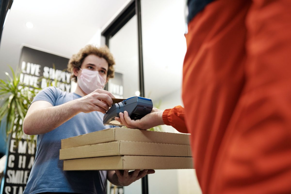 man wearing a face mask paying for pizza delivery